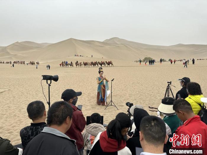 圖為2023年4月底，敦煌大漠“逐舞者”奧楠在鳴沙山月牙泉景區(qū)視頻直播，吸引游人圍觀?！●T志軍 攝
